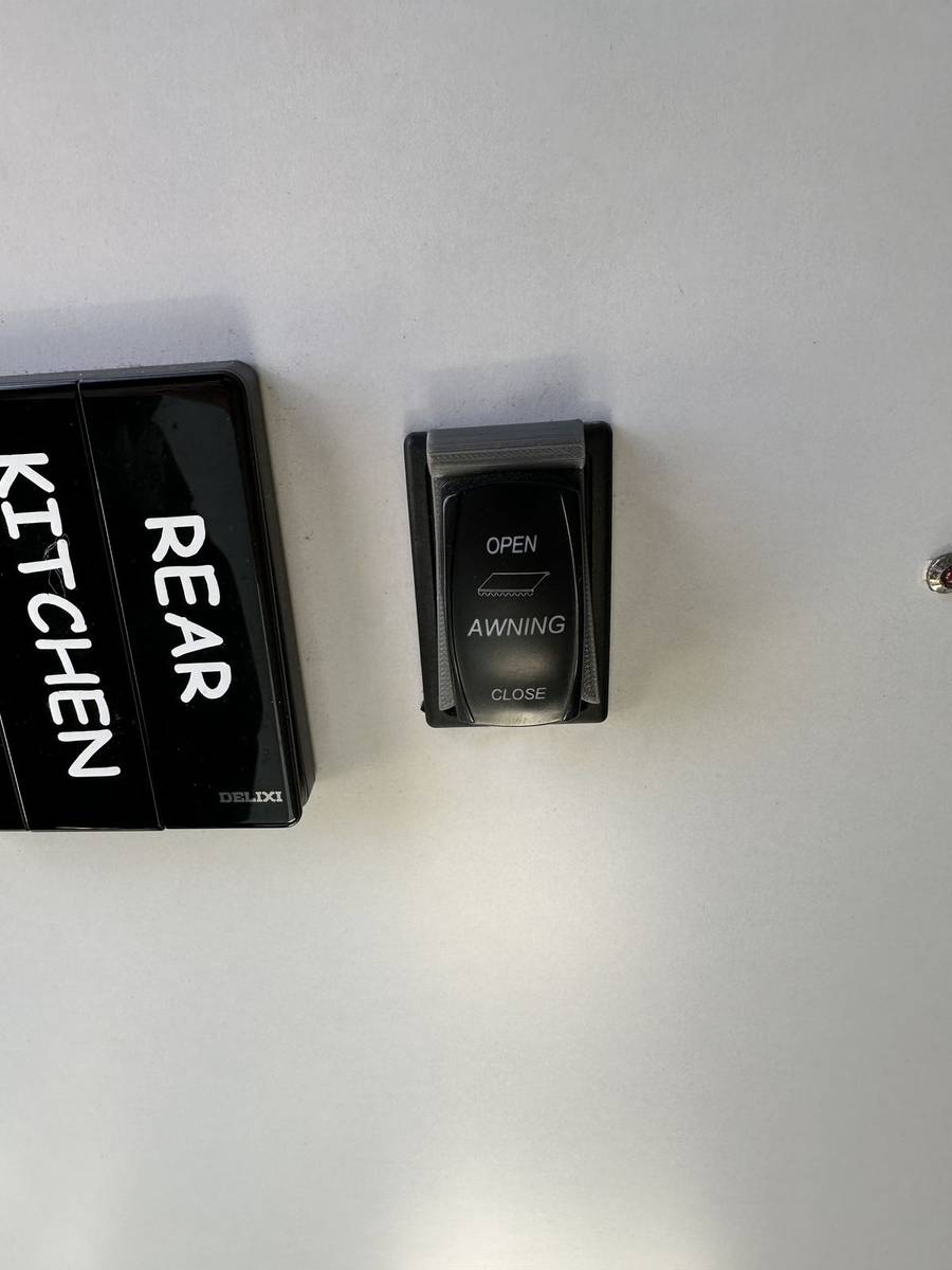 Grey 3D-printed awning switch stopper fitted around a black Scout 15 rocker switch